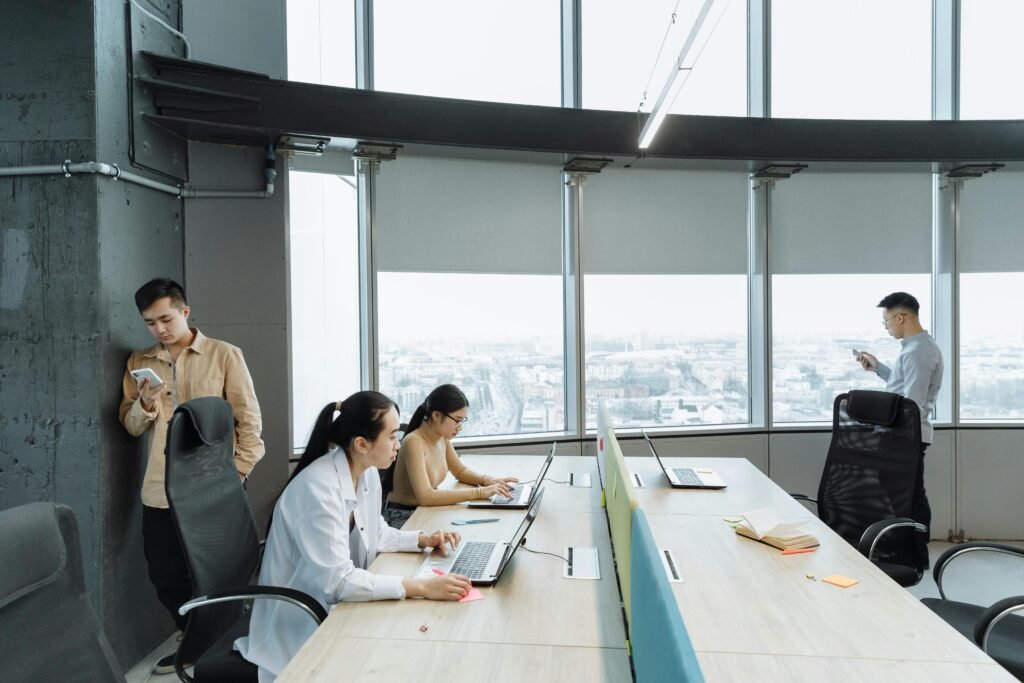Contemporary office scene with Asian coworkers working on laptops and smartphones.